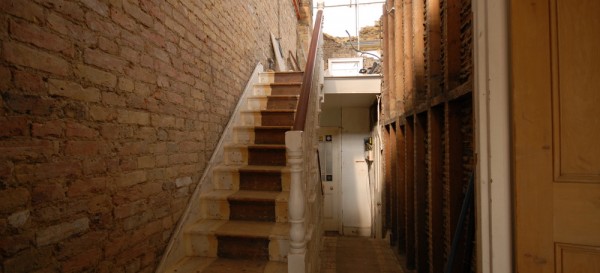 Stairwell where the walls have been hacked back to bare brick and studwork